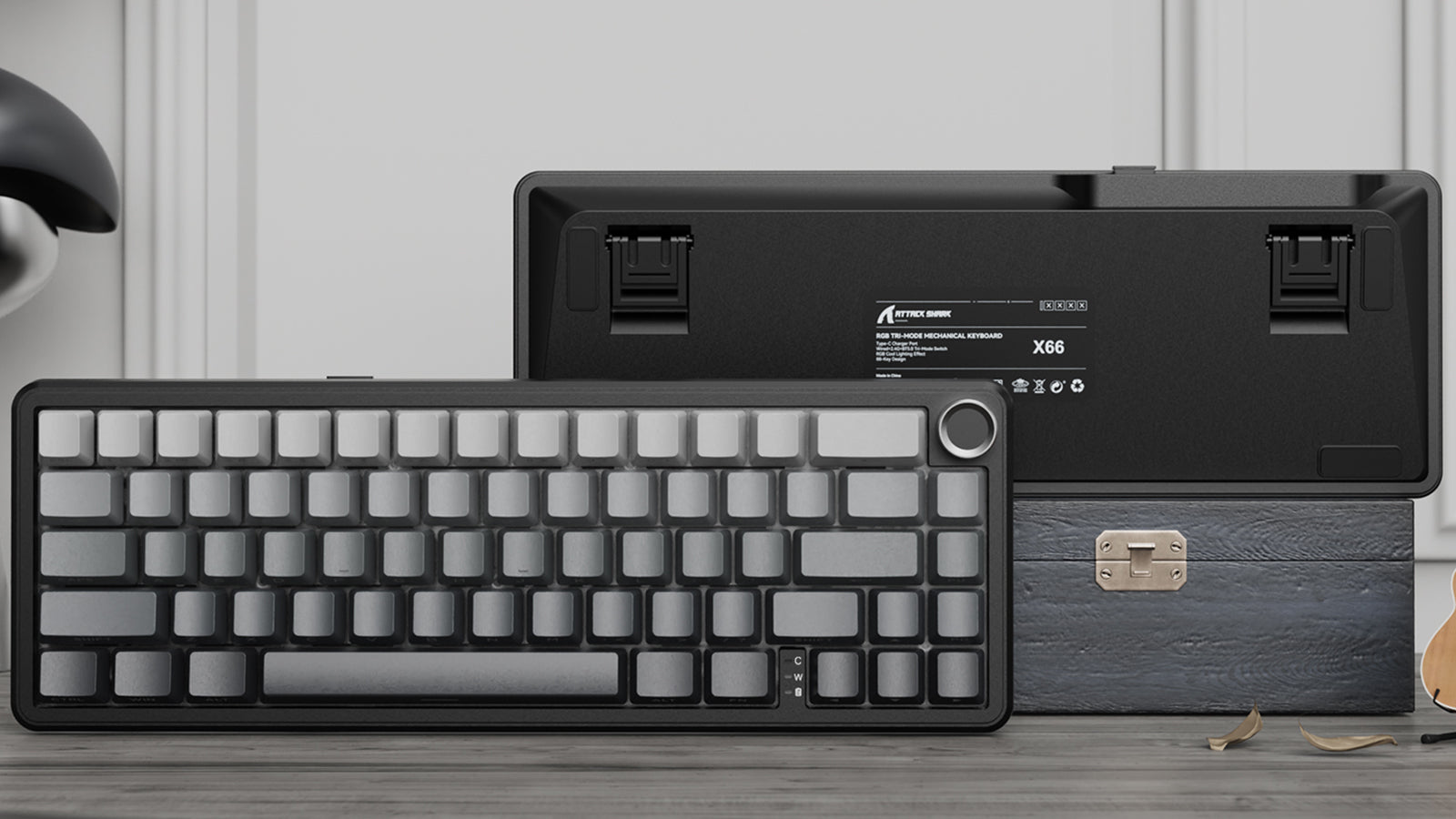 Front and back view of a grey mechanical keyboard with a knob, resting against a textured box.